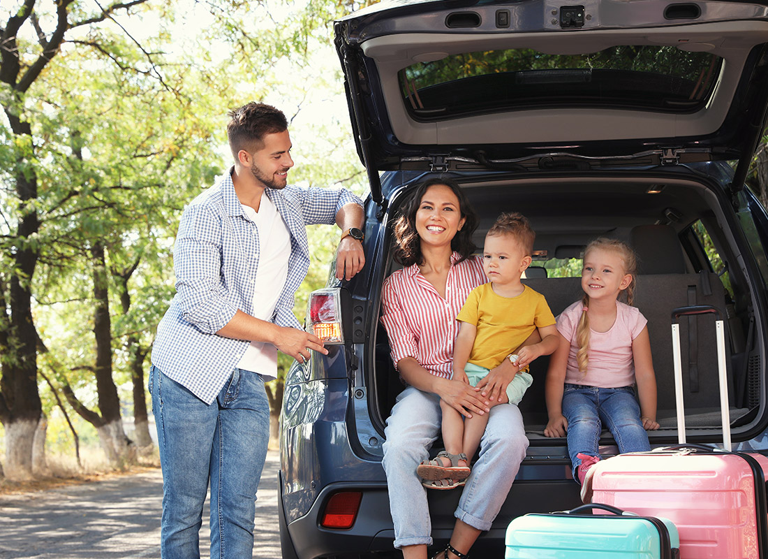 Personal Insurance - Happy Family Sitting in the Back of Their Car With Luggage as the Father Happily Looks at Them