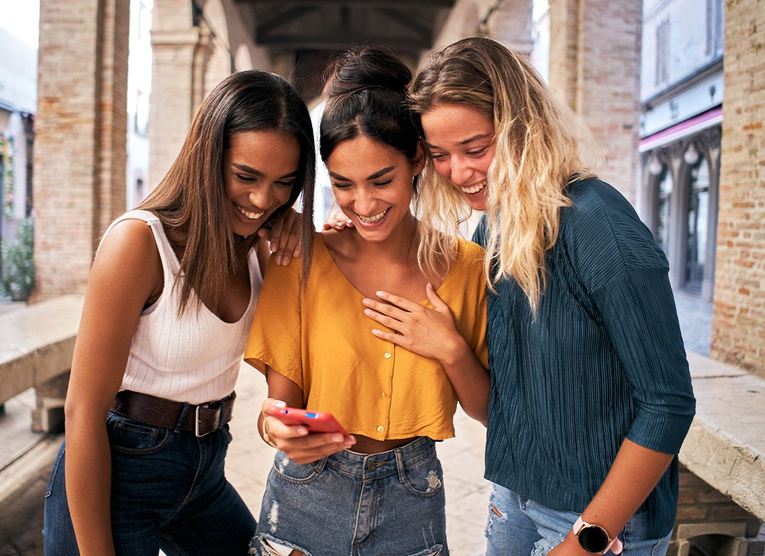Peer Insurance Brokers - Three Happy Women Using Mobile Phone Outdoors on a Bust City City Sidewalk